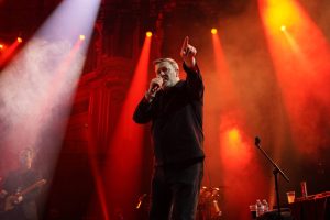 Глядзіце, як Elbow пачынае серыю канцэртаў Teenage Cancer Trust Роберта Сміта ў Каралеўскім Альберт-Холе, калі Гай Гарві распавядае, што фронтмэн The Cure аднойчы «зрабіў нам самы дзіўны камплімент у гісторыі»